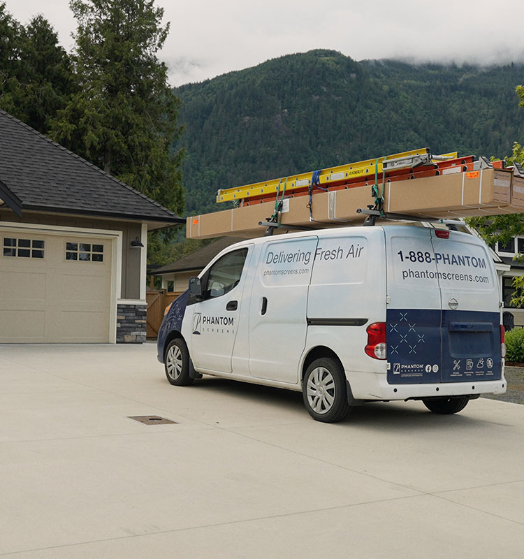 Phantom Screens service van with roof ladders parked in driveway of beige house, mountains visible in background