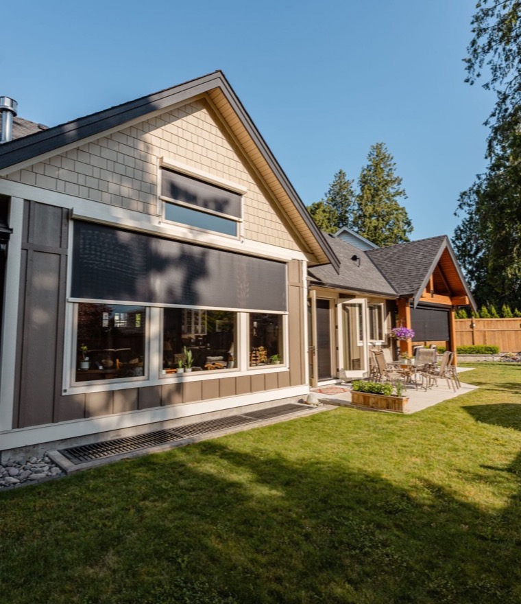 Exterior of a home with solar screens lowered over large picture windows on a sunny day