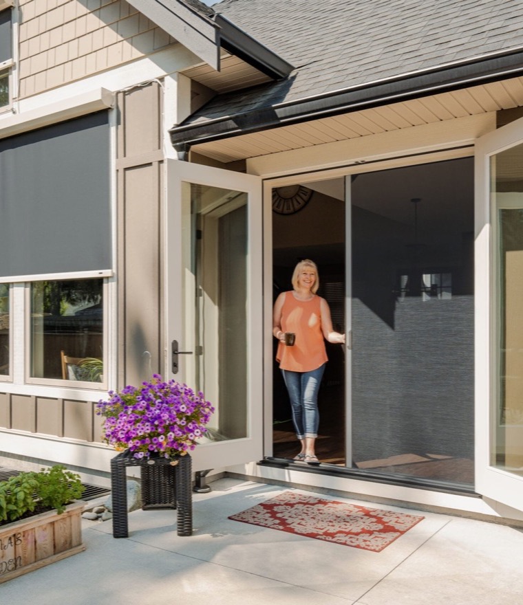 Woman holding a mug in an open patio doorway with a retractable screen, beside windows fitted with exterior solar screens