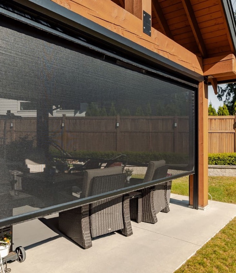 Black solar screen lowered on a timber-frame covered patio with wicker chairs behind it