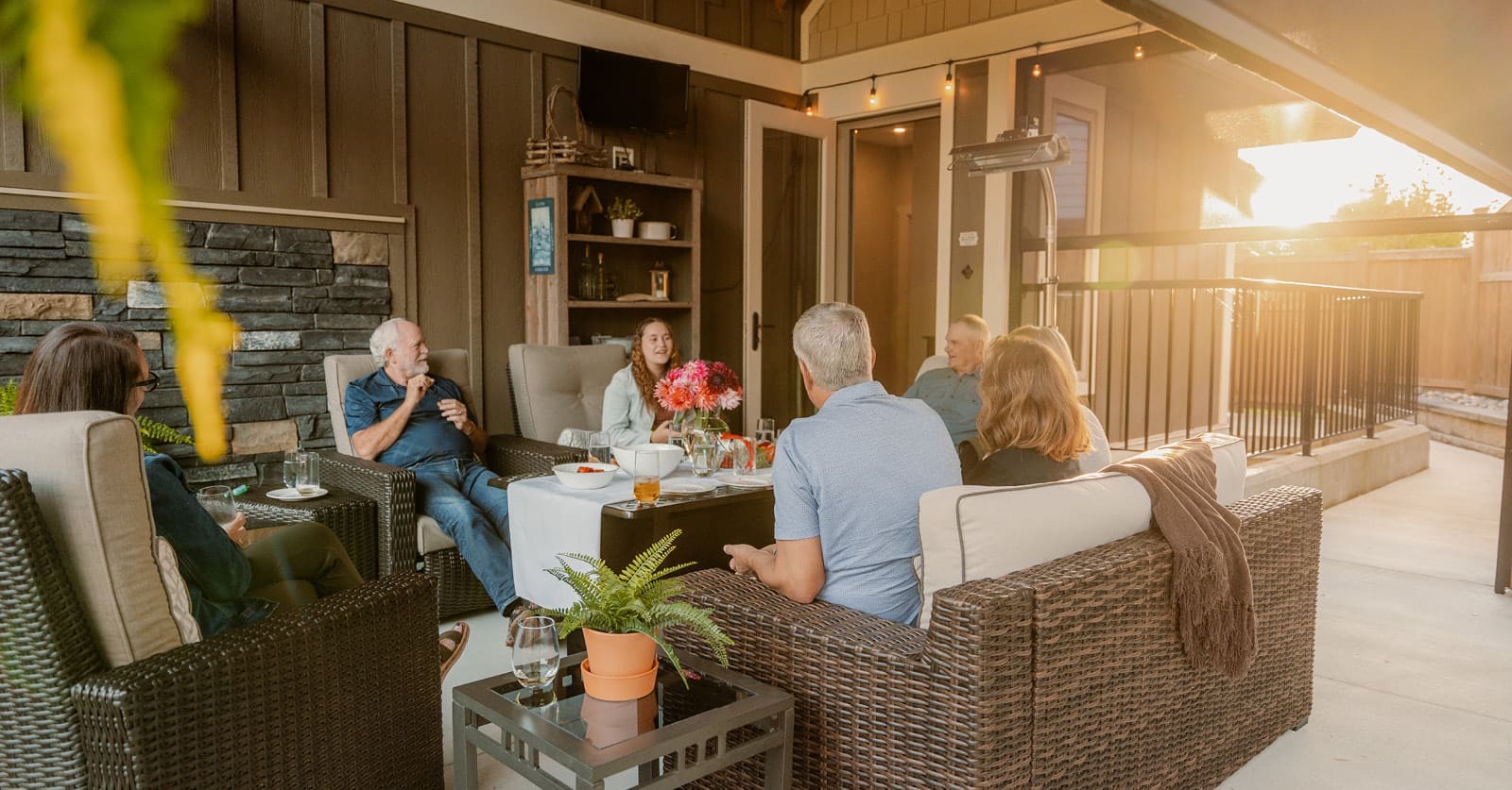 Friends and family relaxing on wicker sofas on a covered patio at sunset