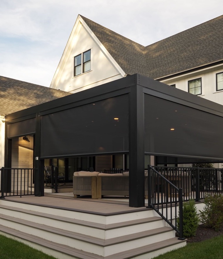 Modern pergola with dark motorized screens lowered on every side at dusk, with lounge seating inside