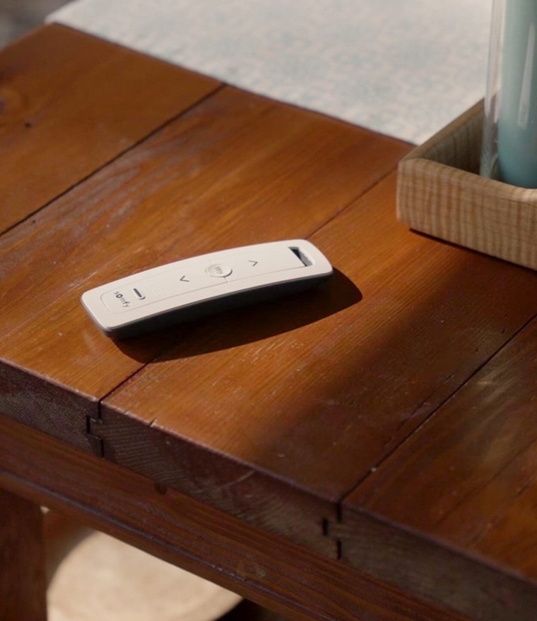 Somfy remote control resting on a rustic wooden coffee table beside a tray of candles