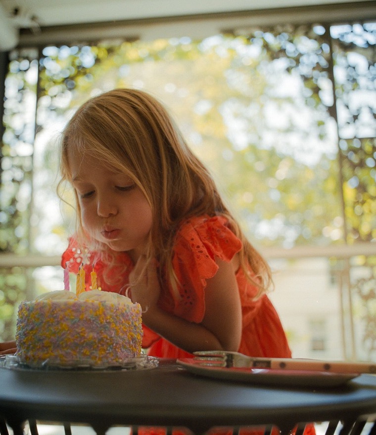 Young girl blowing out candles on a birthday cake on a screened porch surrounded by trees