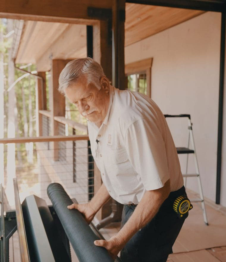Technician installing black mesh screen material on wooden deck