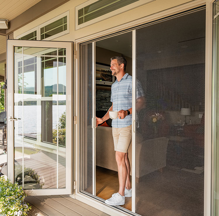 Man standing in a doorway holding coffee, with a retractable screen pulled across the open patio entrance.