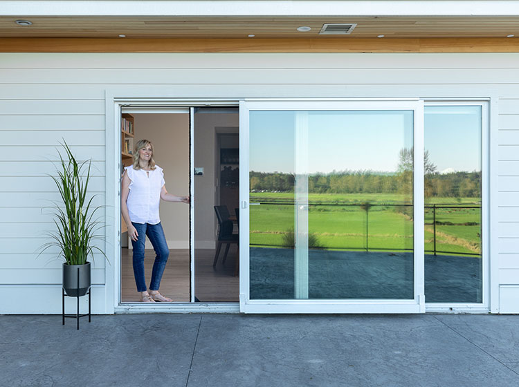 Large sliding glass doors with retractable screen, showing woman in doorway with scenic green field view