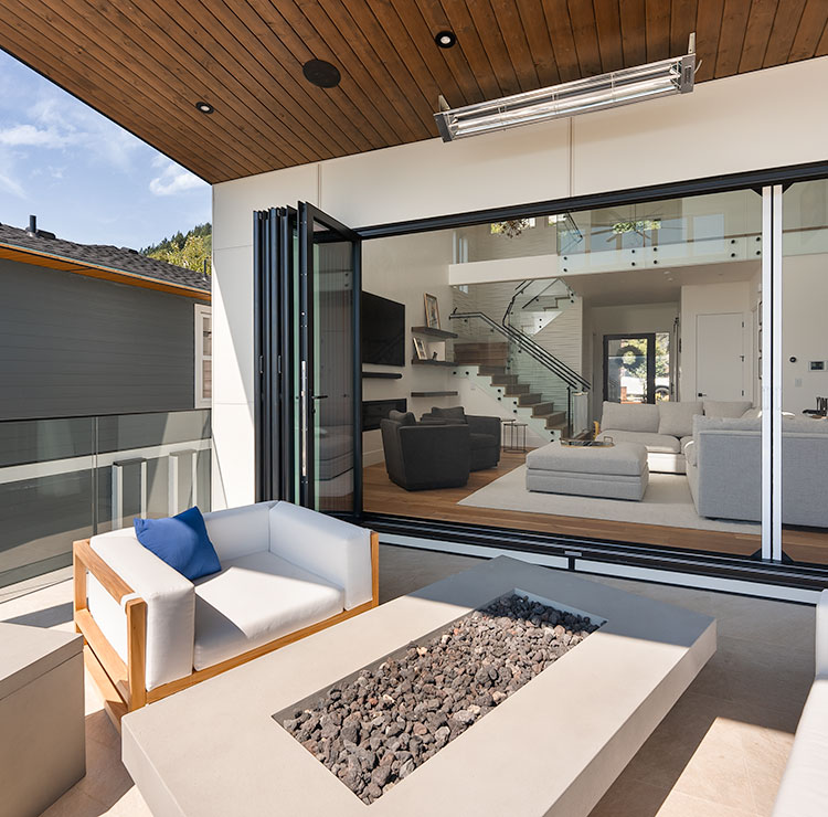 Modern balcony with folding glass door system, white outdoor loveseat, and built-in stone fire pit