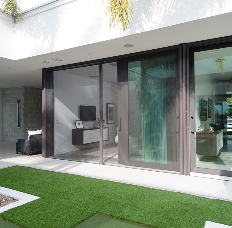 Modern tropical patio with large sliding glass doors, artificial turf, and palm trees framing the space
