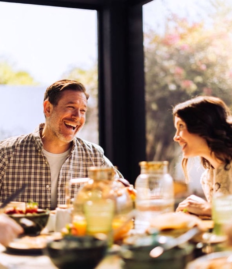 Family laughing around an outdoor dining table on a screened patio on a sunny morning