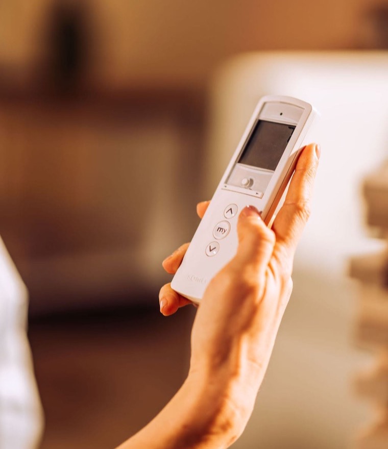 Close-up of a hand holding a white Somfy &lsquo;my&rsquo; remote control indoors