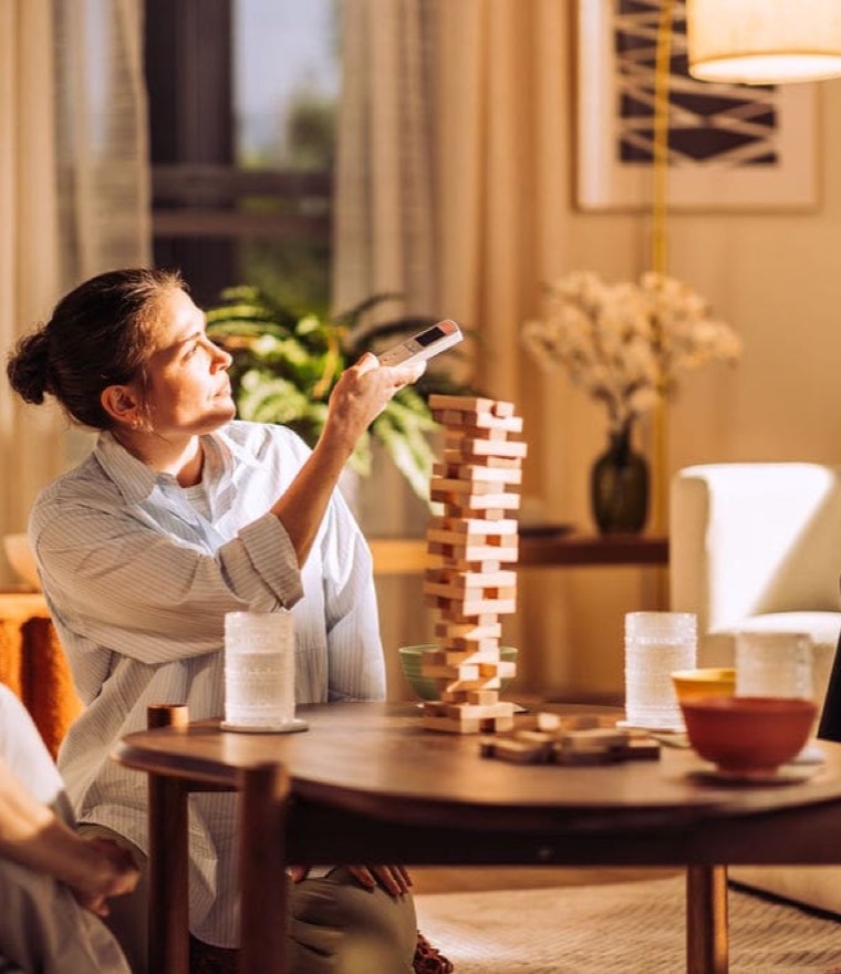 Family playing a block-stacking game in a cozy living room while a woman lowers a motorized screen with a remote