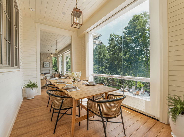 Elegant outdoor dining area on screened porch with wooden table and rattan chairs overlooking lush garden views