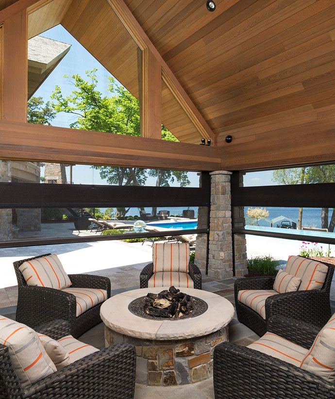 Elegant outdoor pavilion with retractable screens showcasing a stone firepit seating area and pool view