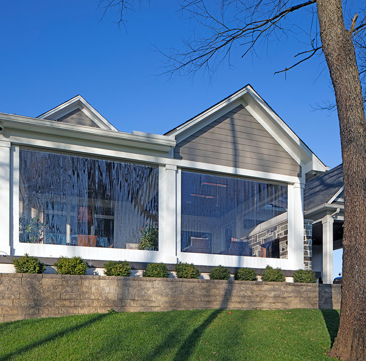 Elevated home exterior with clear vinyl screens spanning large porch openings, showcasing seamless integration with white trim