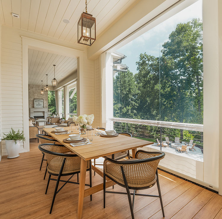 Elegant screened porch with wooden dining table and rattan chairs, natural light streaming through clear vinyl panels