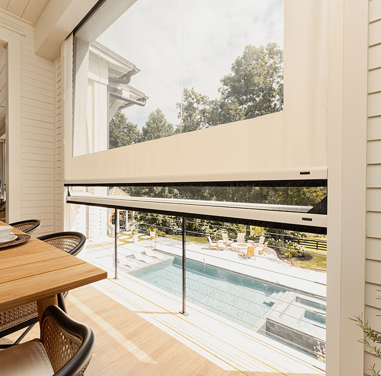 Partially retracted vinyl screen system revealing pool view, showcasing modern outdoor dining setup with cable guides