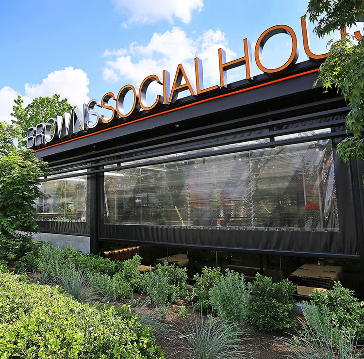 Restaurant storefront with retractable vinyl screens, modern signage, and landscaped entrance