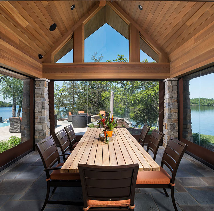 Lakefront dining pavilion with clear vinyl screens, wooden table, and panoramic water views
