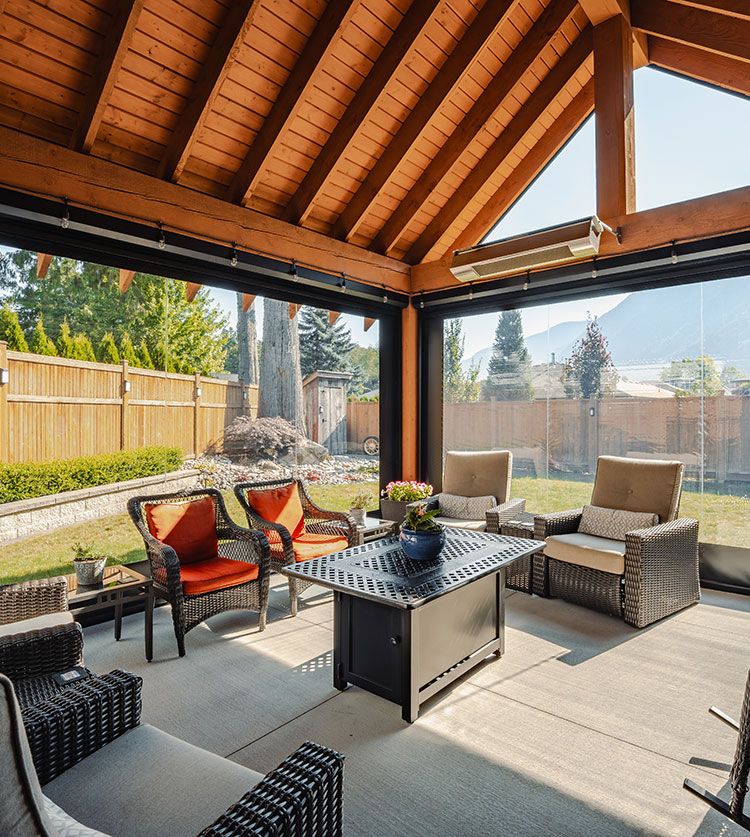 Covered patio with motorized screens, featuring wicker furniture with gray and orange cushions, fire table, and mountain views through clear vinyl panels
