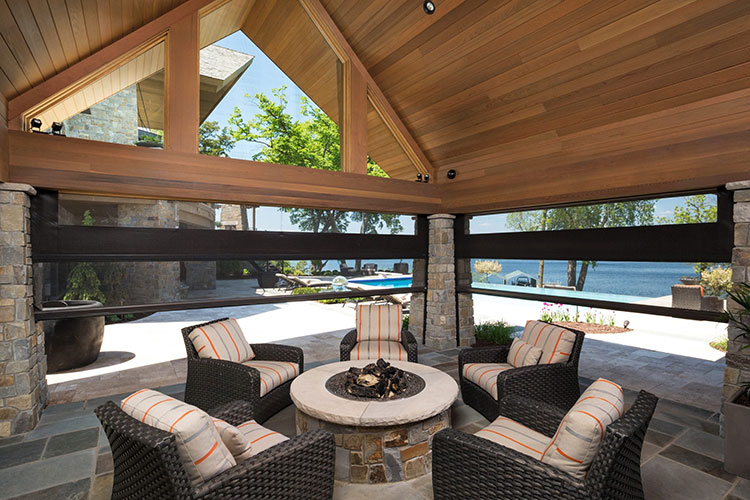 Covered patio featuring dual roller system with both mesh and vinyl screens, mounted between stone columns with firepit seating area