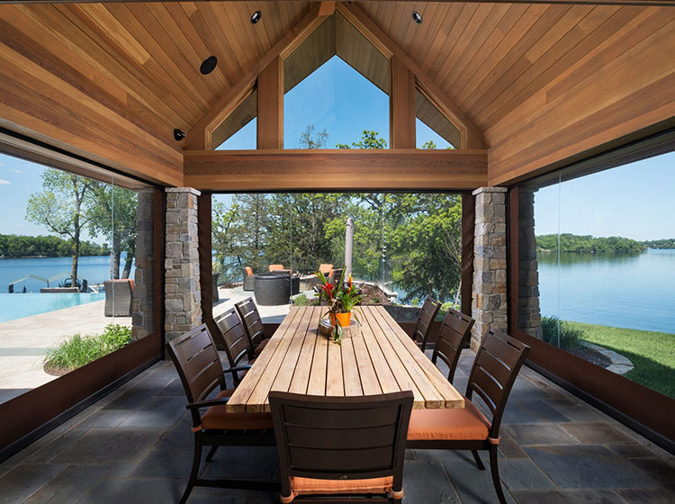Lakeside dining pavilion with retractable screens, wooden ceiling, and stone columns overlooking water view