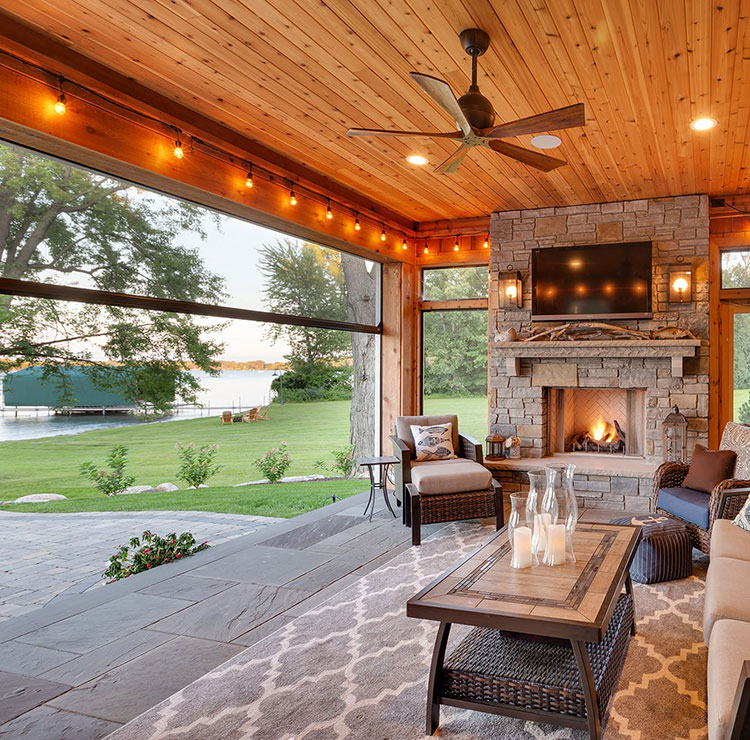 Cozy screened porch with stone fireplace, string lights, and lakefront view through retractable screens
