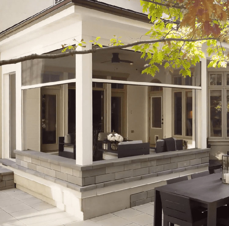 White modern patio with stone base and motorized screens, featuring outdoor dining and built-in grill