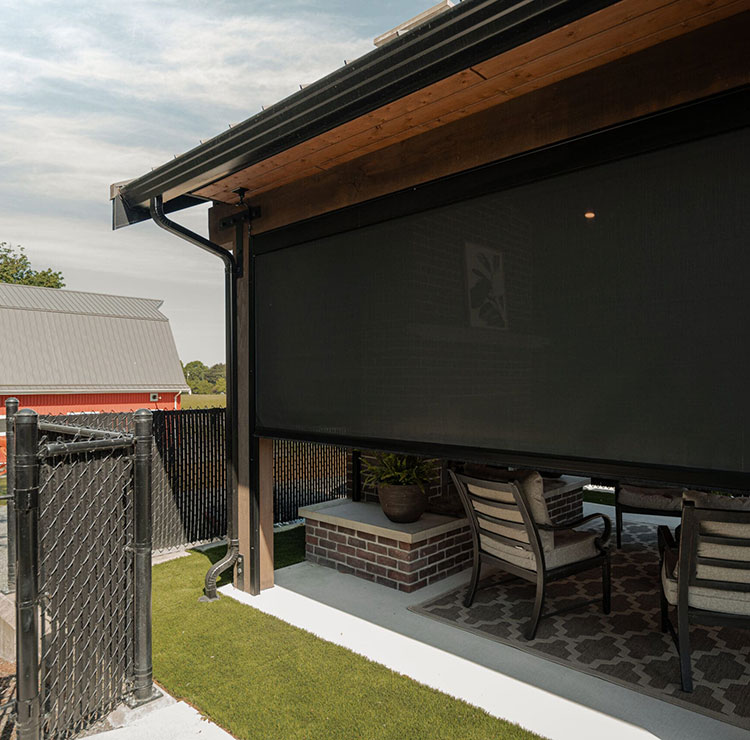 Covered patio with dark motorized screen, outdoor seating, and view of red barn in background