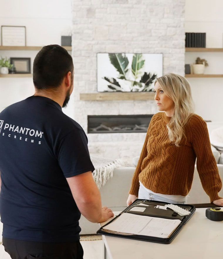 Phantom Screens employee consulting with a homeowner at a kitchen counter with paperwork and samples
