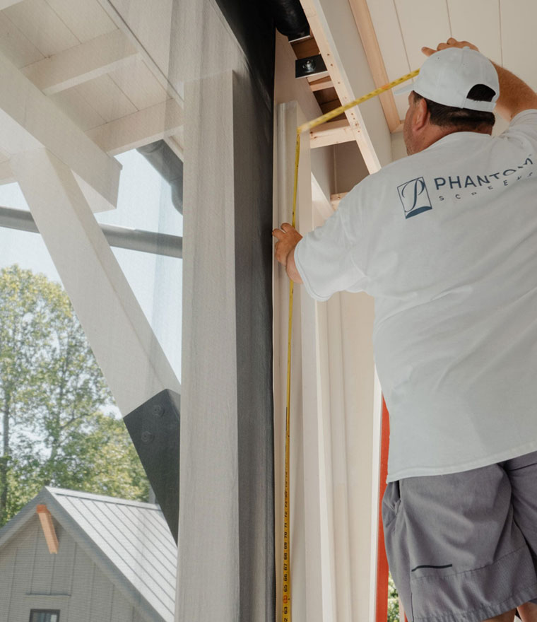 Installer using a tape measure on a retractable screen track on a covered porch