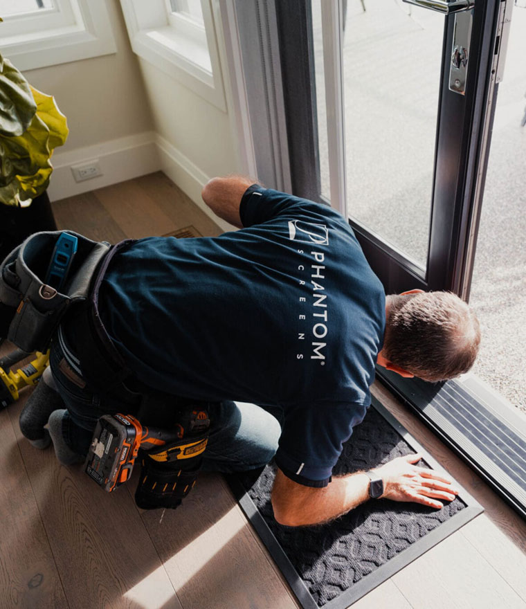 Installer kneeling at a sliding door, securing the bottom track of a retractable screen