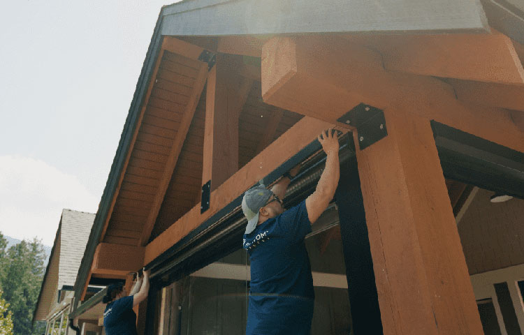 Two installers mounting a motorized screen housing on a covered patio
