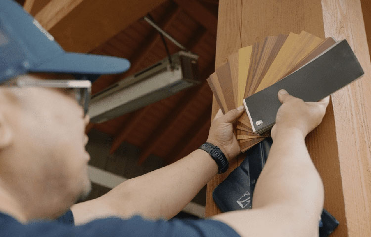Hands holding wood grain color swatches next to a retractable screen