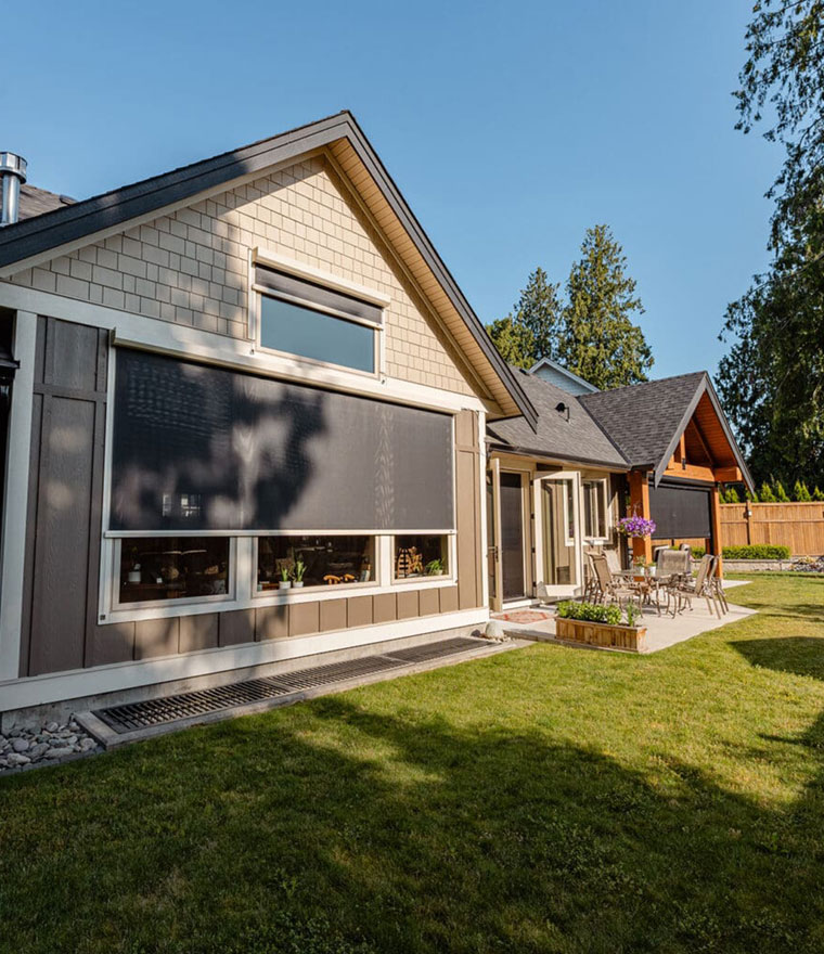 Exterior of a home with large dark solar screens covering windows, backyard visible