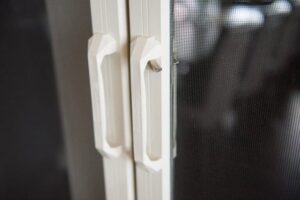 Close-up of a white door handle on a glass door, designed for a Phantom Screens retractable door system.